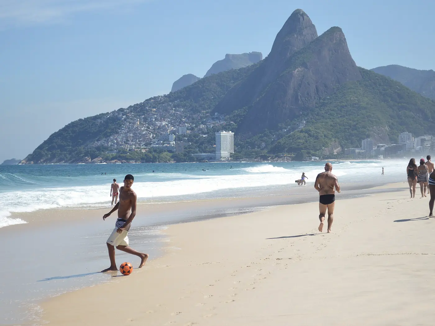 Gente caminando y jugando en la playa de Ipanema, con el morro Dois Irmãos al fondo